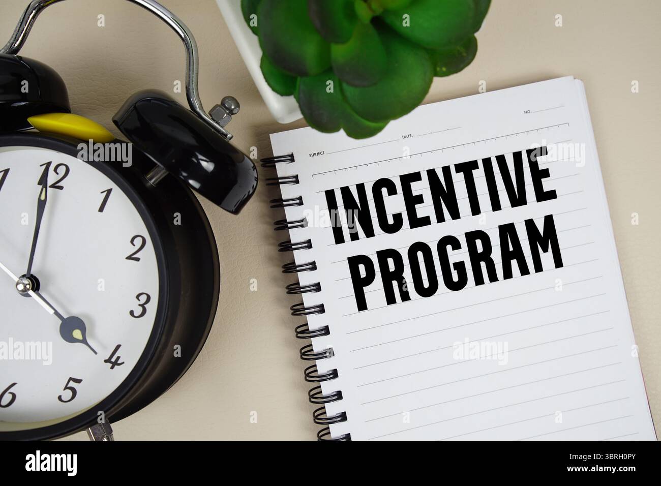 Testo del programma di incentivazione scritto sul blocco note con sveglia Foto Stock