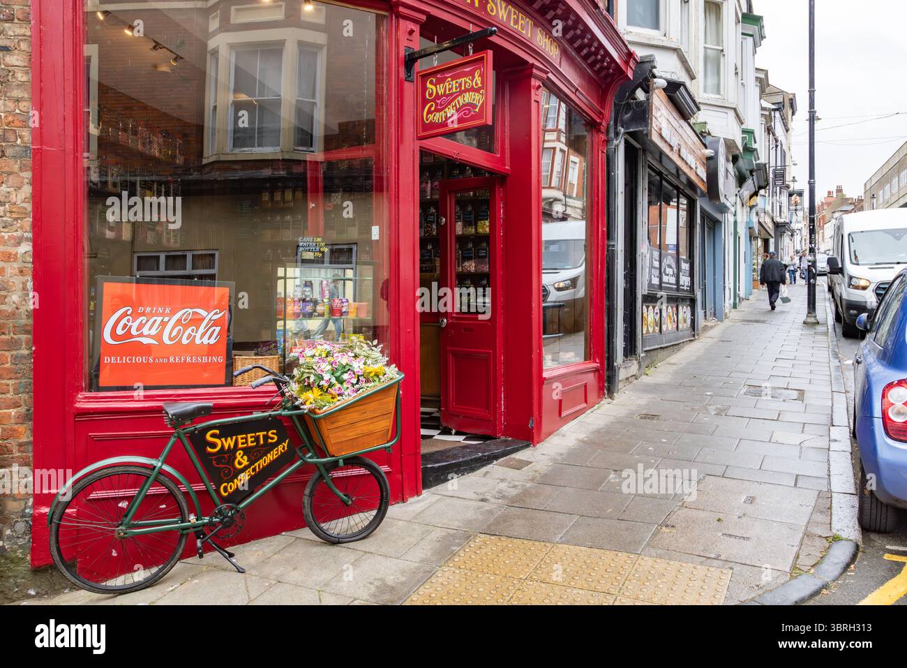 Tradizionale negozio di dolci con bicicletta vintage e cartello Coca-Cola su una strada principale britannica, che attrae il turismo nostalgico e i temi del commercio al dettaglio. Foto Stock
