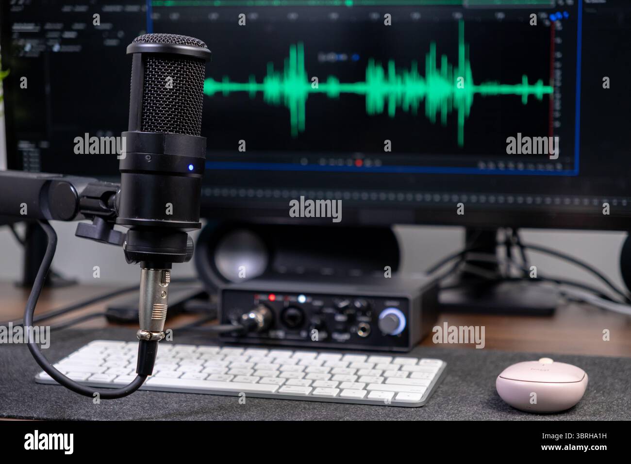 Primo piano del microfono a condensatore nero e dell'interfaccia audio sulla scrivania, con forme d'onda sonore verdi su un monitor, che mette in risalto i podcast e la musica moderni Foto Stock