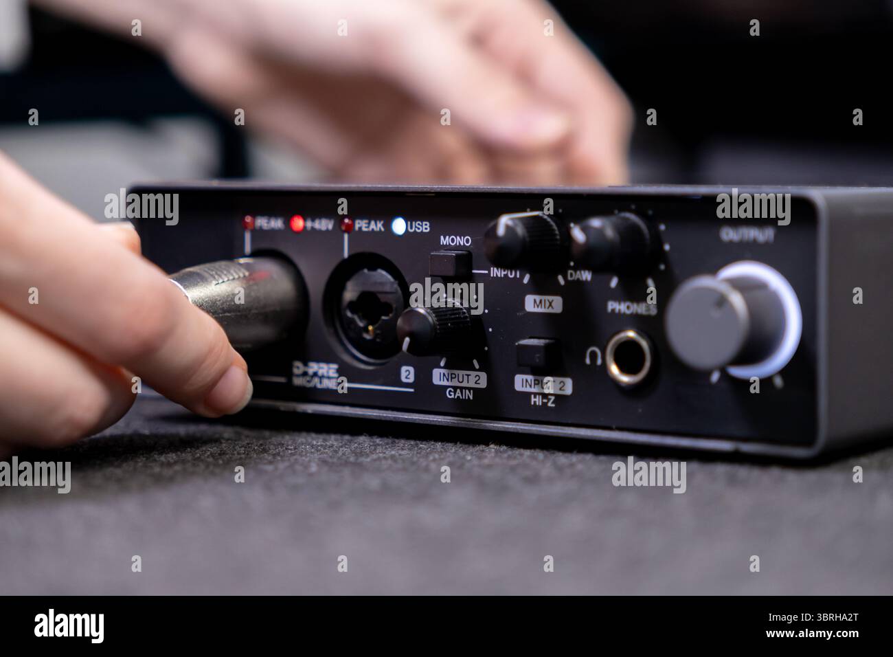 Mano di una persona che inserisce un cavo per microfono XLR in un'interfaccia audio da studio, fondamentale per la produzione di musica di alta qualità, lo streaming live e i podcas Foto Stock Mano di una persona che inserisce un cavo per microfono XLR in un'interfaccia audio da studio, fondamentale per la produzione di musica di alta qualità, lo streaming live e i podcas Foto Stock