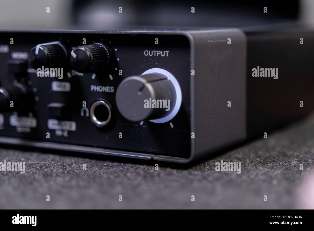 Interfaccia audio scura con manopola di uscita illuminata e jack per cuffie, accessori essenziali per mixaggio audio, podcasting e aud digitale Foto Stock