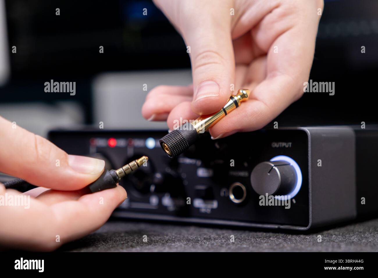 Primo piano di una mano inserendo un adattatore jack audio placcato oro in un'interfaccia, sottolineando il collegamento audio per la creazione di musica o studi professionali Foto Stock