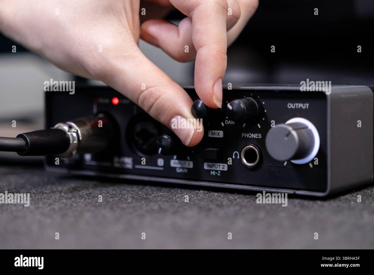 Scatto dettagliato di un individuo che regola la manopola di controllo su un mixer audio digitale nero, ottimizzando l'uscita audio per la creazione di contenuti creativi o strea Foto Stock