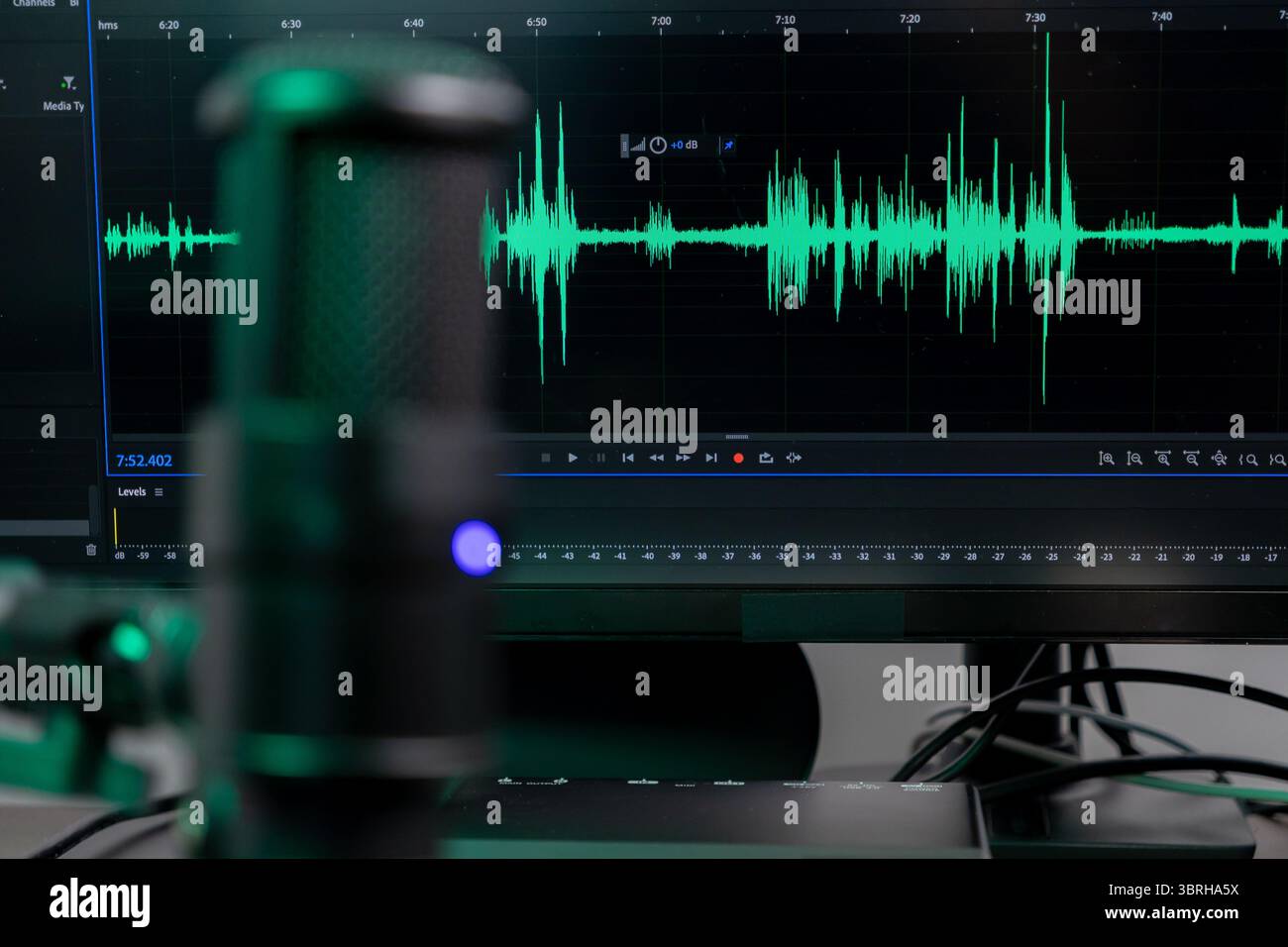 Forma d'onda audio verde brillante sul monitor e microfono da tavolo professionale, che presenta una configurazione da studio per la registrazione audio e la creazione di contenuti Foto Stock