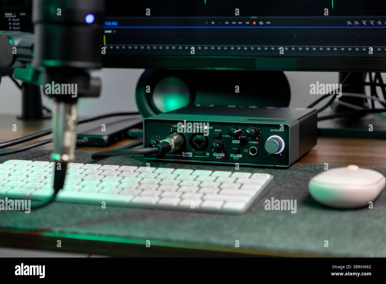 Visualizzazione dettagliata di un'interfaccia audio avanzata, microfono e schermo del computer che visualizza le forme d'onda, catturando l'essenza della creazione di contenuti digitali Foto Stock