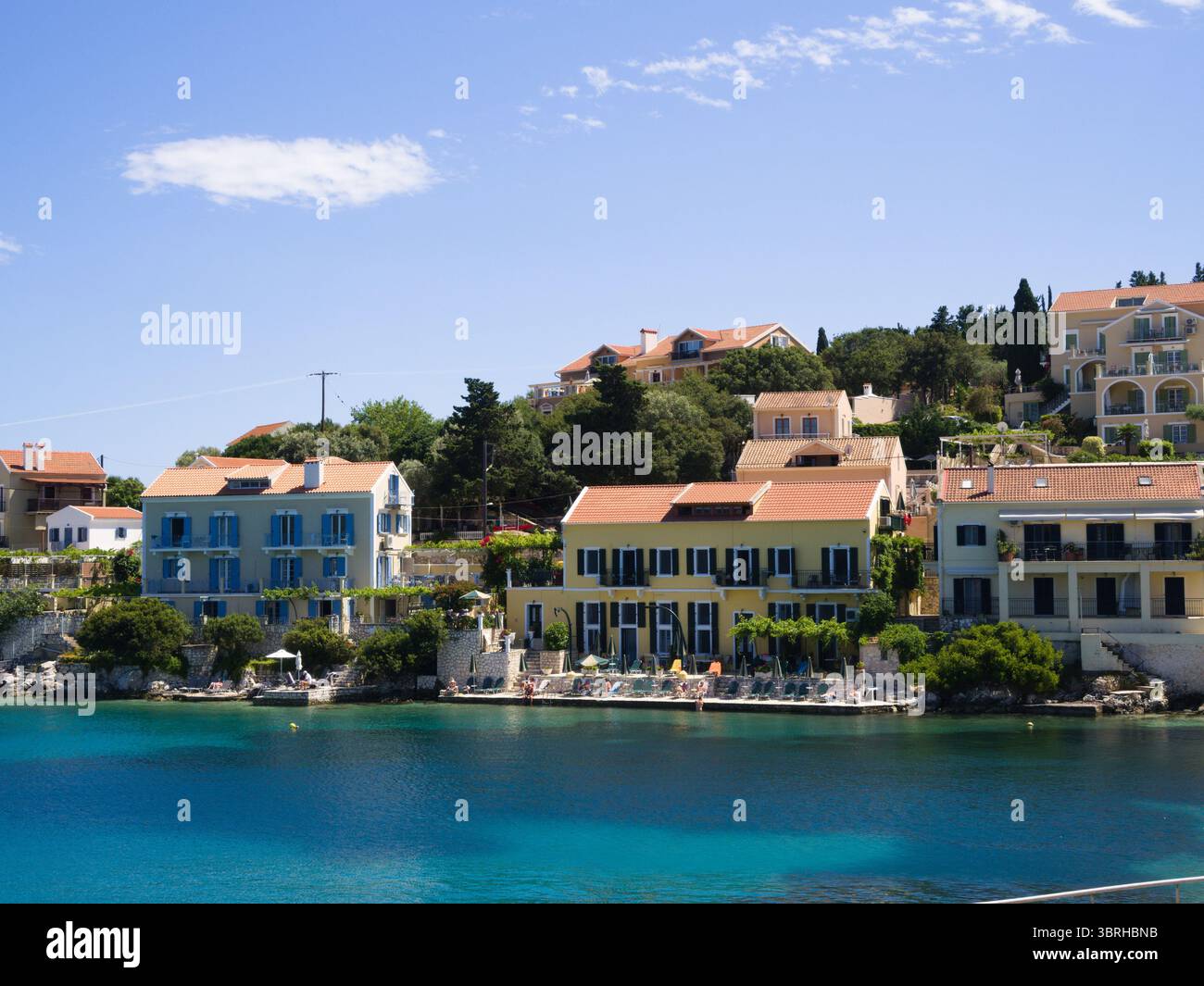 Tradizionali case costiere del villaggio di Fiskardo con il mare calmo di fronte. Un tranquillo e colorato porto dell'isola greca. Foto Stock
