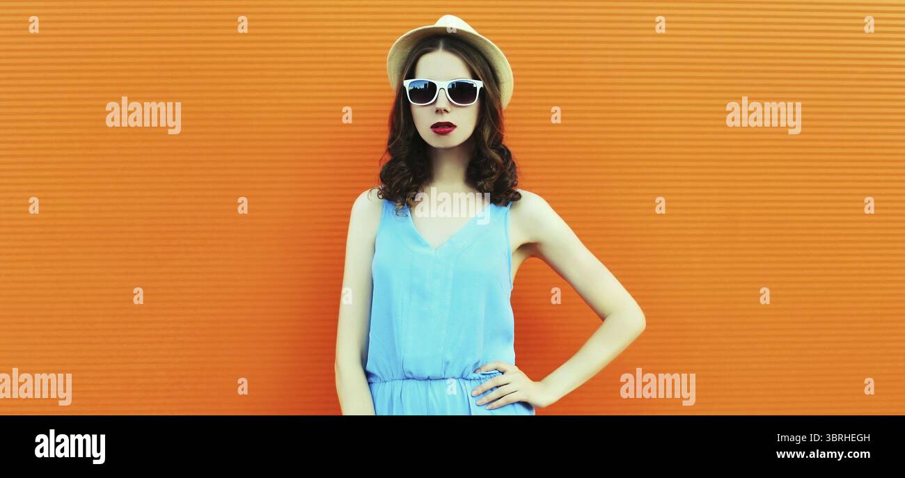 Ritratto di una giovane donna che posa indossando un cappello estivo, vestito su sfondo arancione Foto Stock