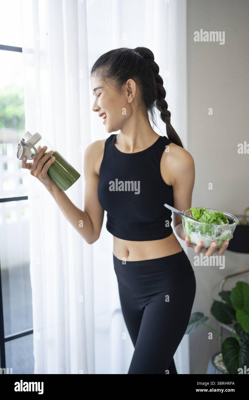Fitness donna asiatica che mangia insalata sana e beve frullato verde organico disintossicazione alla frutta per la dieta dopo allenamento allenamento allenamento in studio di yoga healt Foto Stock