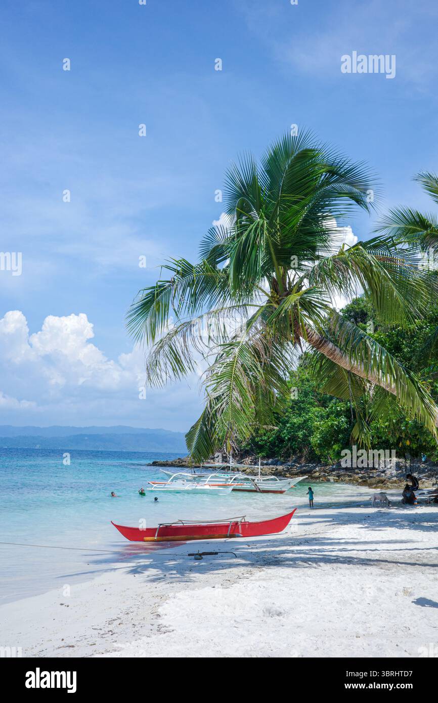 Una splendida vista costiera della remota spiaggia di sabbia bianca con palme e barche tradizionali nelle Filippine. Una vita isolana rilassata di Palawan Foto Stock
