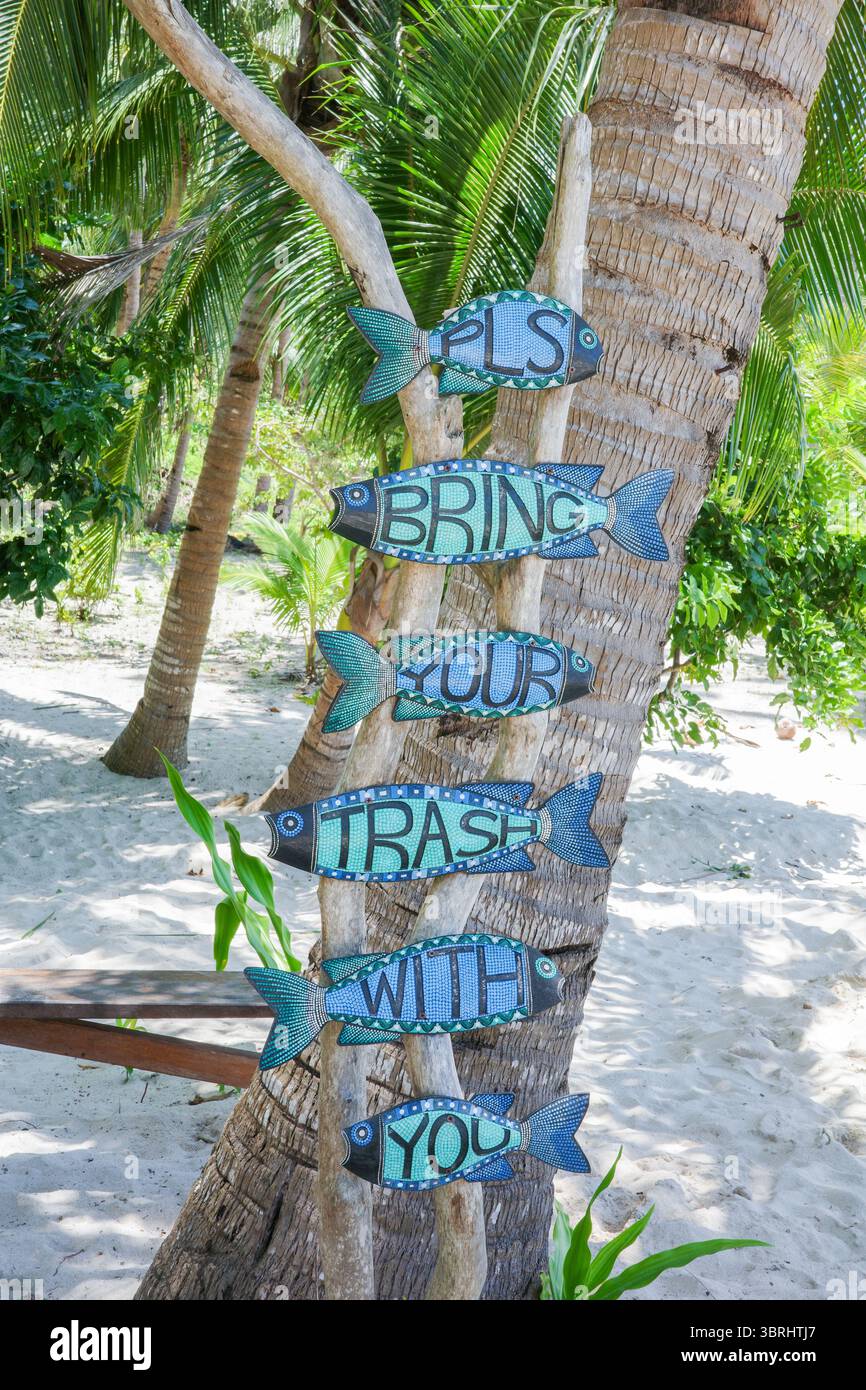 Un cartello creativo fatto a mano su un albero di cocco presenta colorate forme di pesce di legno con il messaggio: "PLS porta la spazzatura con te" in un Eco-Friendlyec Foto Stock