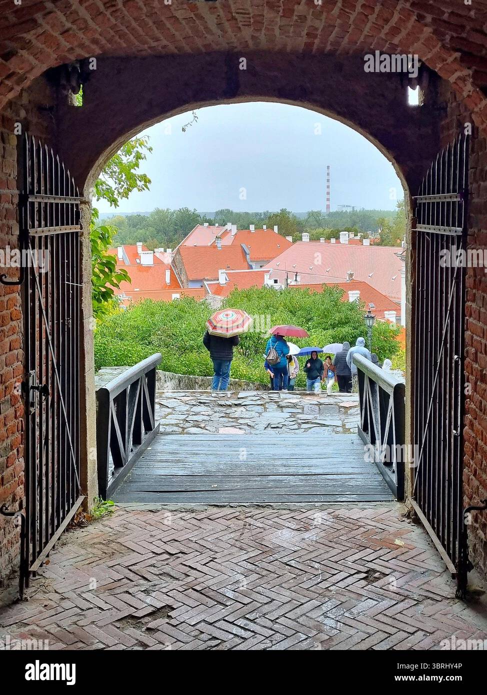 Vista panoramica attraverso le porte ad arco dell'antica fortezza fino ai tetti di tegole rosse e alle persone con ombrelli a Petrovaradin, Serbia Foto Stock