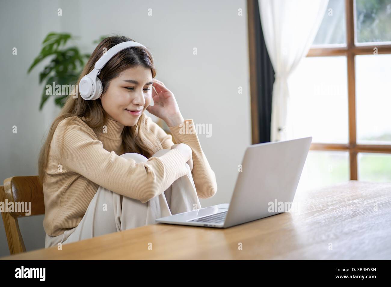 Bella e felice donna asiatica che indossa le cuffie che usa il computer portatile al lavoro o che si gode la musica Foto Stock