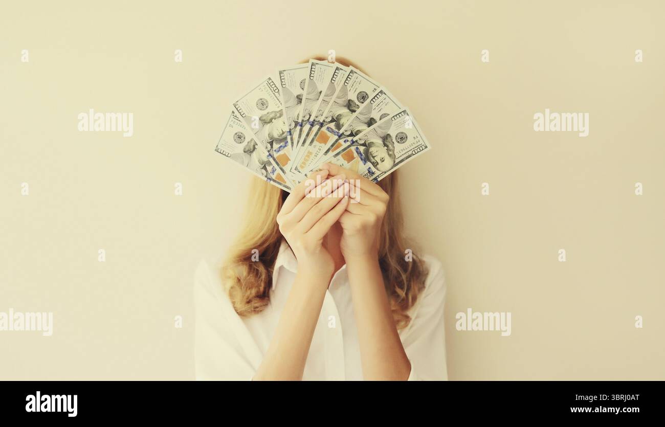 Ritratto di una donna felice che tiene in mano soldi in contanti in banconote da un dollaro che le copre il viso Foto Stock