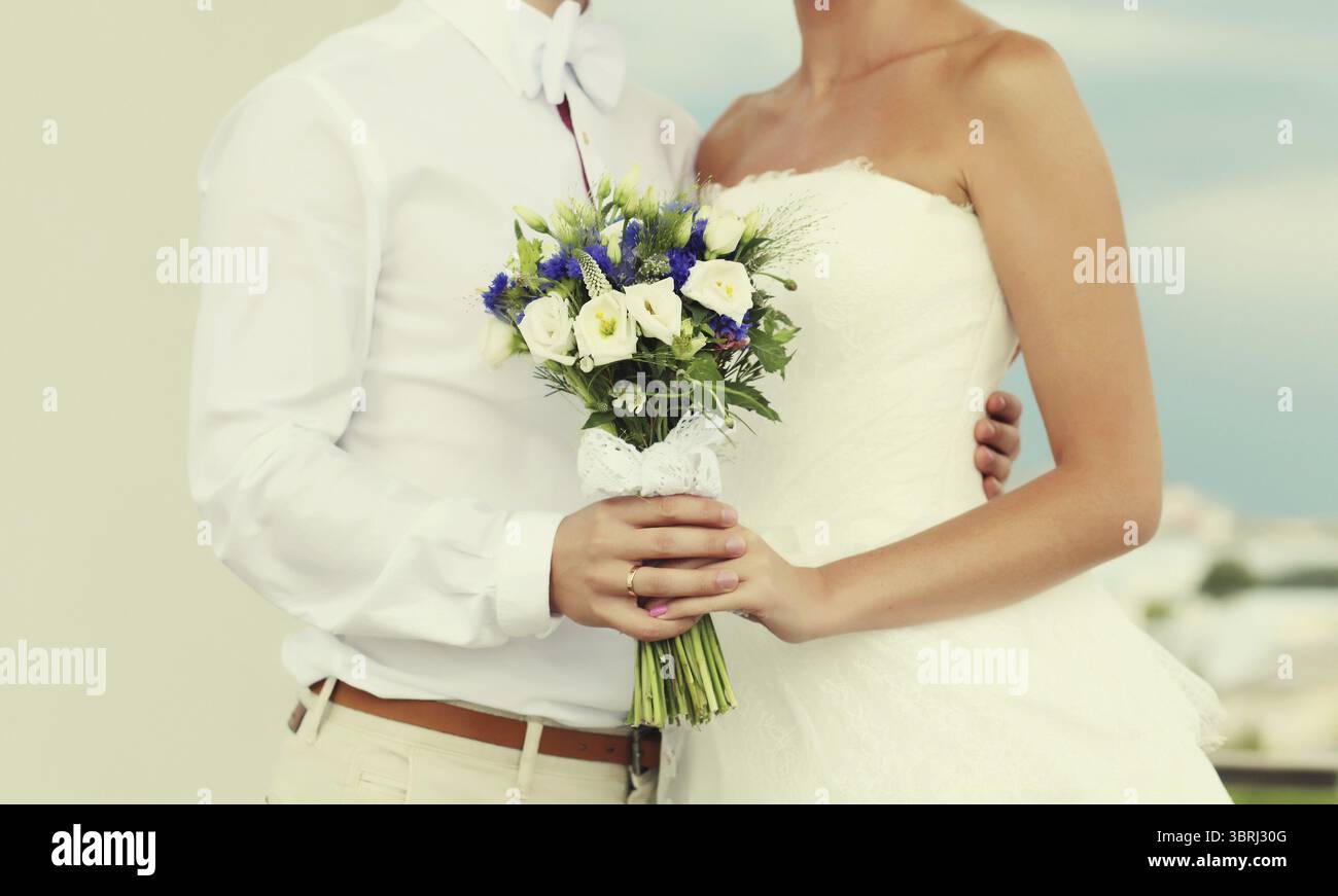 Coppia di nozze, sposa in abito bianco con bouquet di fiori e sposo in camicia che tiene per mano all'aperto Foto Stock