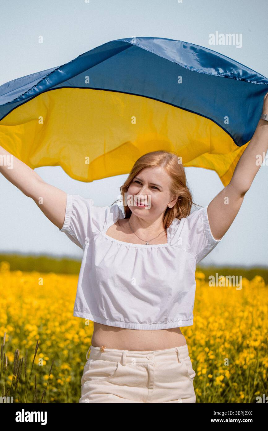 Ritratto di donna che esprime orgoglio nazionale con bandiera Ucraina tra fiori di colza gialli in onore del giorno della bandiera Foto Stock