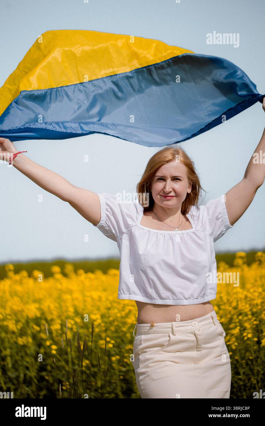 Ritratto di donna che esprime orgoglio nazionale con bandiera Ucraina tra fiori di colza gialli in onore del giorno della bandiera Foto Stock