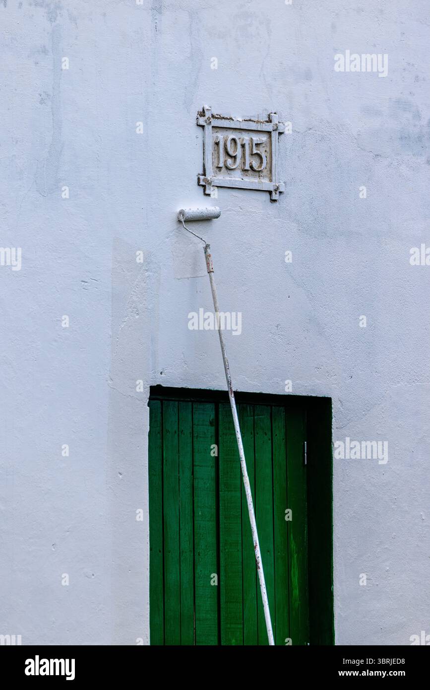un lungo pennello dipinto di bianco dipinge uno splendido edificio restaurato della piantagione di roca con una pietra databile del 1915 sopra una porta di legno verde Foto Stock