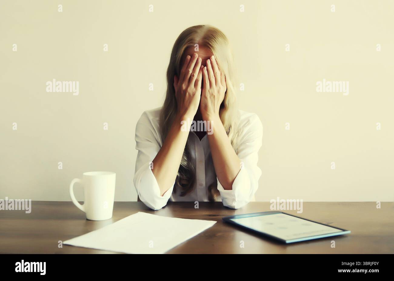 Triste turbato emotivo che piange dipendente mentre lavora con un tablet, documento cartaceo con una tazza di caffè seduto al tavolo di casa Foto Stock