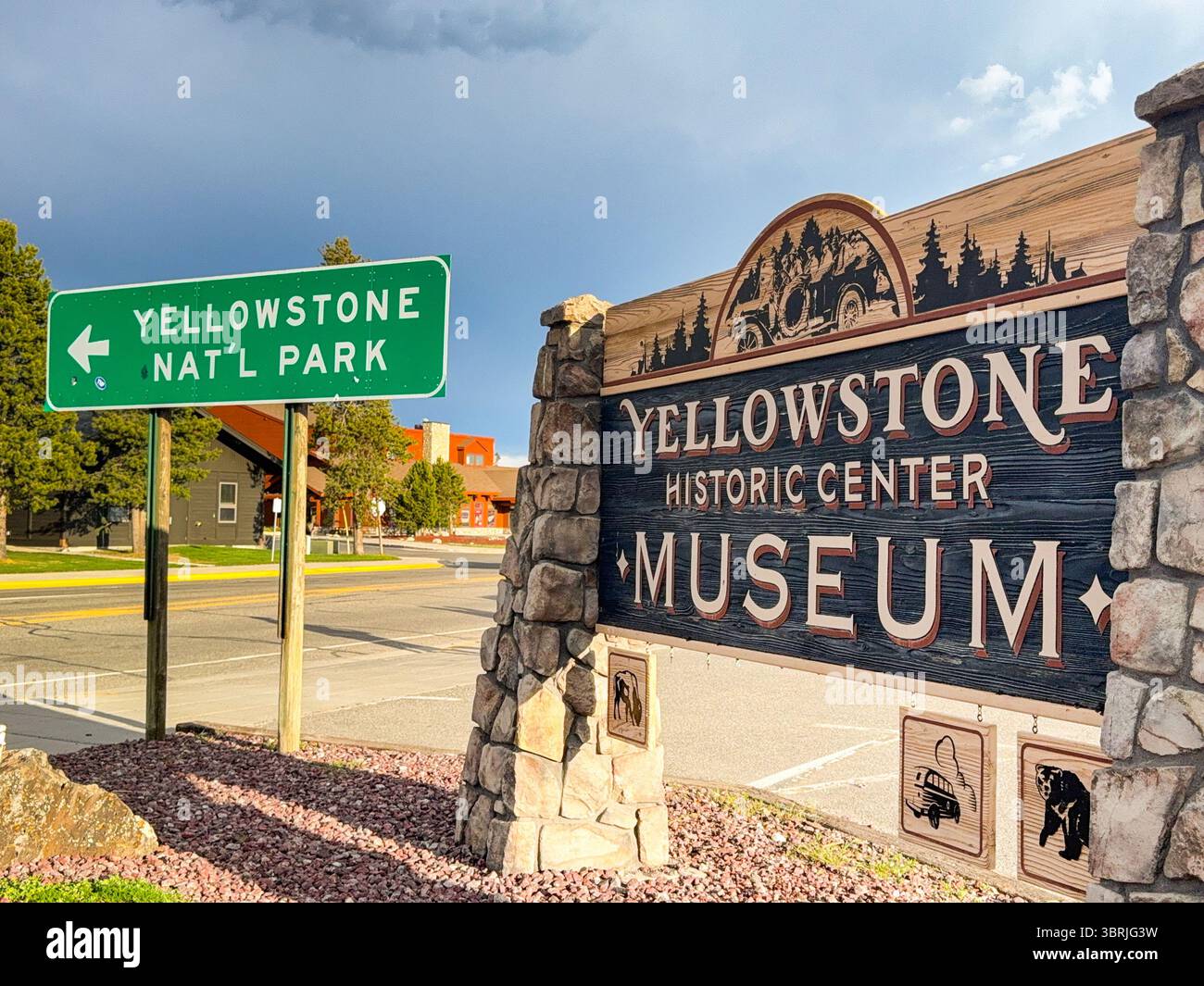 West Yellowstone, Montana, USA - 29 maggio 2025: Cartello stradale per l'ingresso al parco nazionale di Yellowstone e il museo della città sulla strada principale - Immagine stock catturata con smartphone