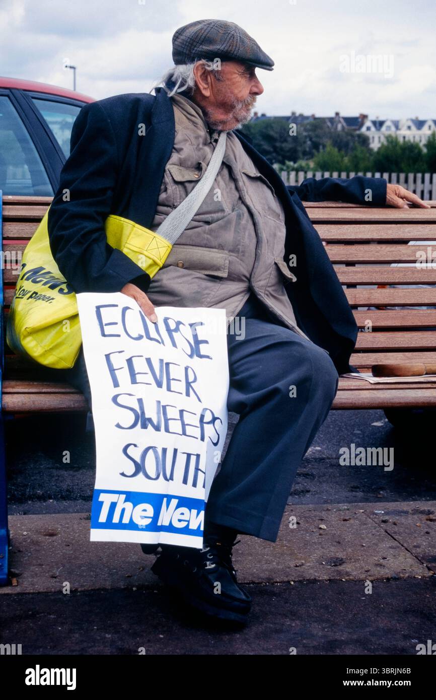 il venditore di giornali anziani sedeva sul panchina sul lungomare tenendo un grande poster scritto a mano con titoli di coda la febbre dell'eclissi spazza verso sud riferendosi all'eclissi solare totale agosto 1999 inghilterra regno unito Foto Stock