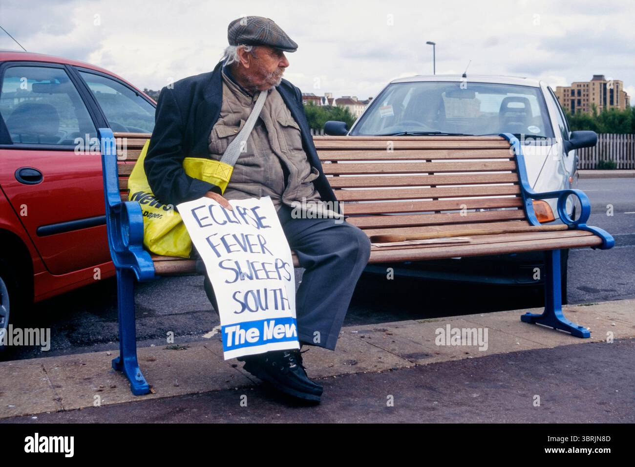 il venditore di giornali anziani sedeva sul panchina sul lungomare tenendo un grande poster scritto a mano con titoli di coda la febbre dell'eclissi spazza verso sud riferendosi all'eclissi solare totale agosto 1999 inghilterra regno unito Foto Stock