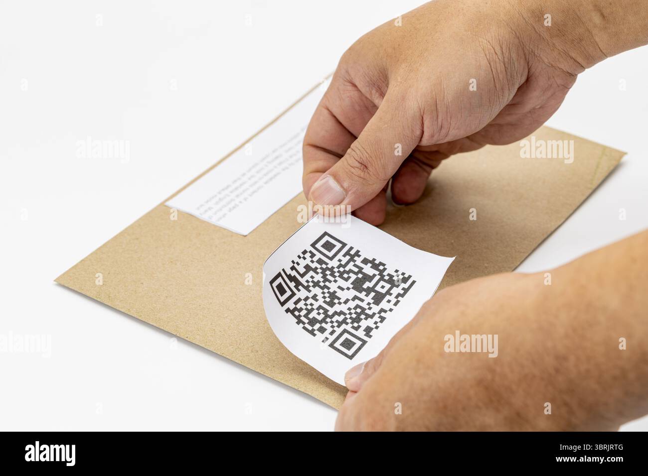 Una persona sta attaccando l'etichetta con codice qr sulla busta marrone, dimostrando un modo moderno ed efficiente di gestire le informazioni. le mani stanno posizionando con attenzione l'etichetta Foto Stock