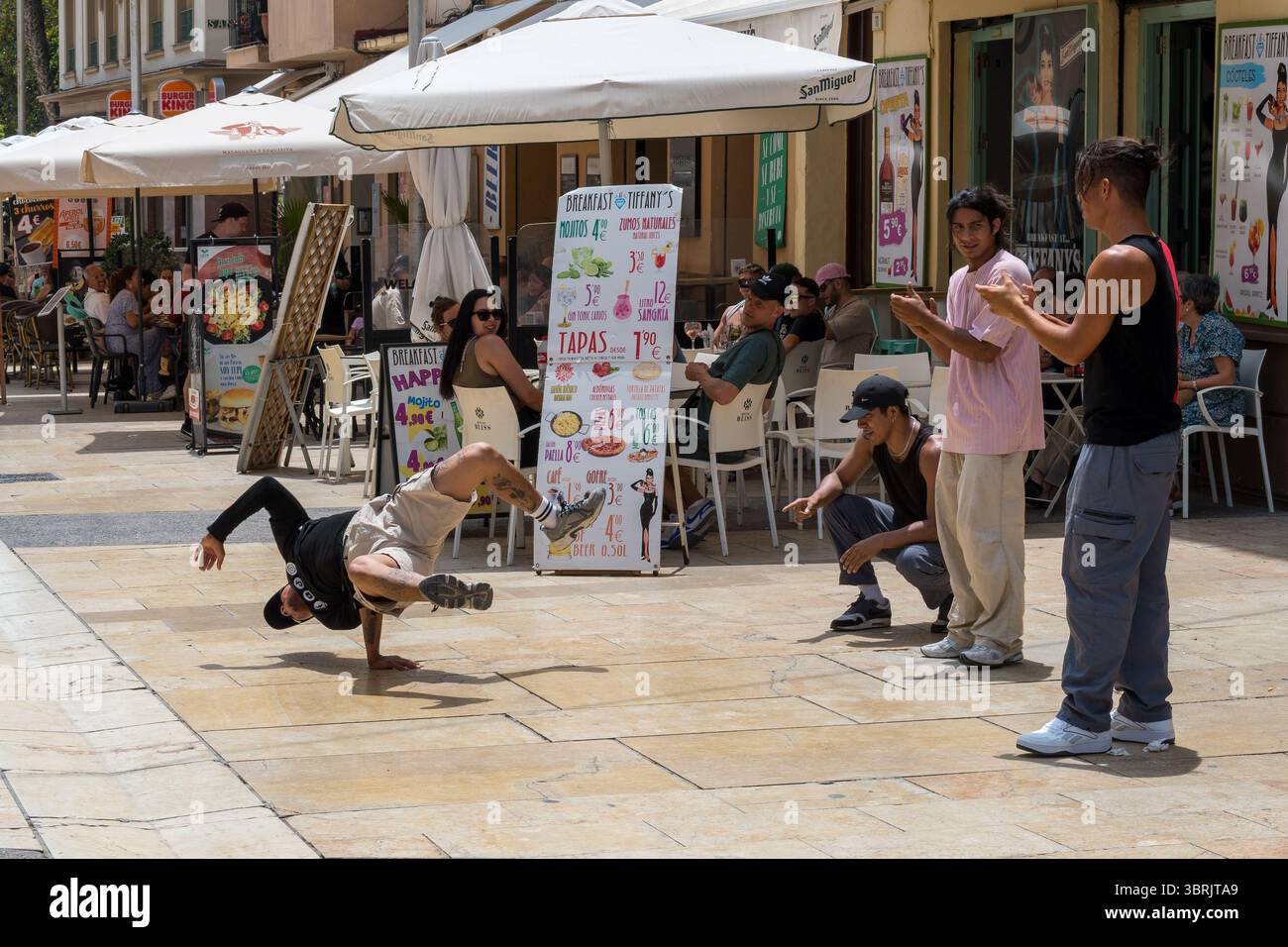 Gli artisti di strada danno energia alla vivace Málaga plaza con movimenti acrobatici e musica, attirando sorrisi dai caffè all'aperto Foto Stock