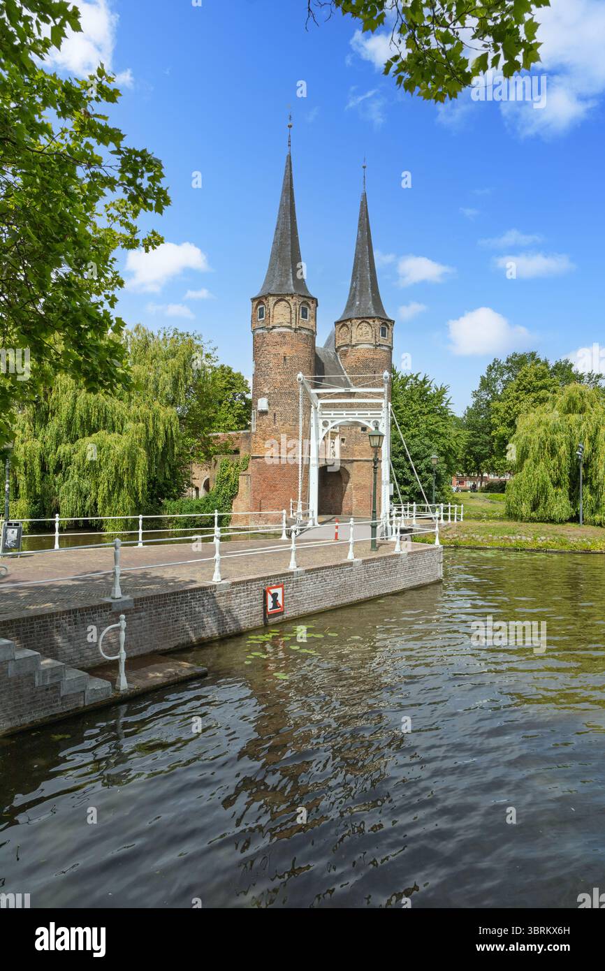 La storica Oostpoort (porta orientale) a Delft, Paesi Bassi, con le sue guglie gemelle, il ponte levatoio e il tranquillo canale, incorniciato da alberi lussureggianti. Foto Stock