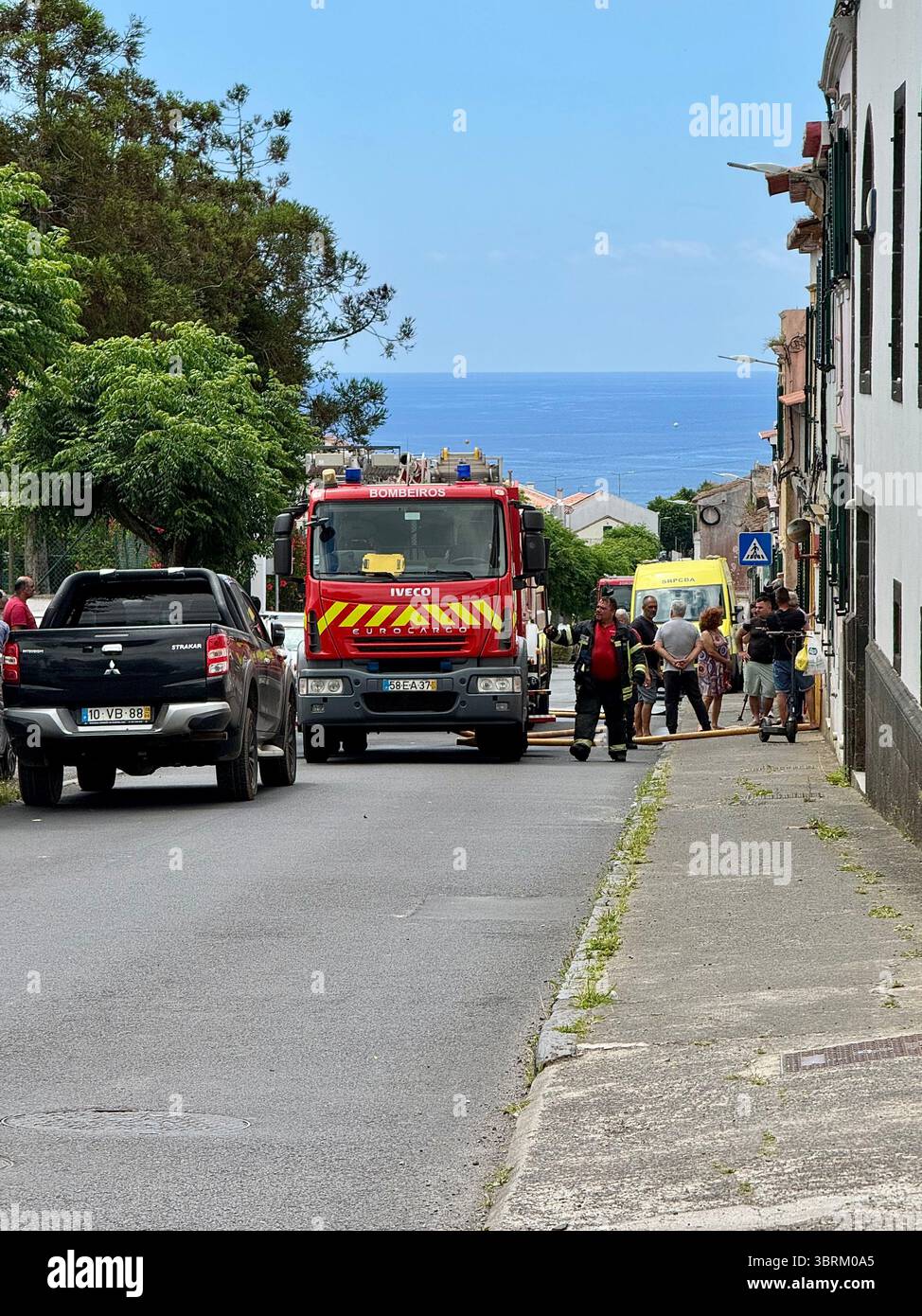 Veicoli di emergenza, tra cui un camion dei vigili del fuoco e un'ambulanza su una strada con vista sull'oceano in una città costiera sull'isola di São Miguel, Azzorre, Portogallo. - Immagine stock catturata con smartphone