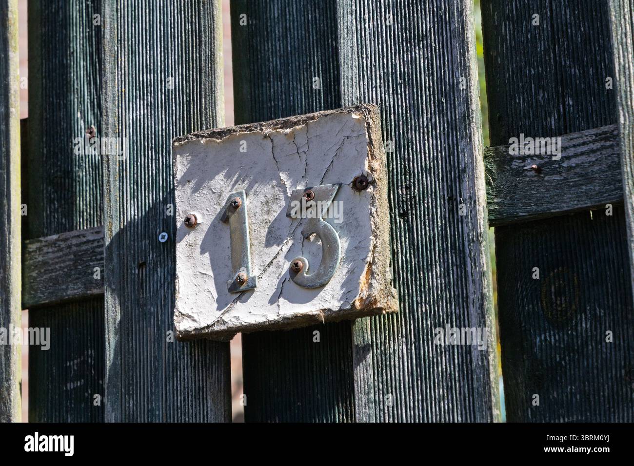 Un numero civico "13" con vernice sbucciante è apposto su una vecchia recinzione in legno testurizzato, catturando un'estetica rustica e invecchiata. Foto Stock