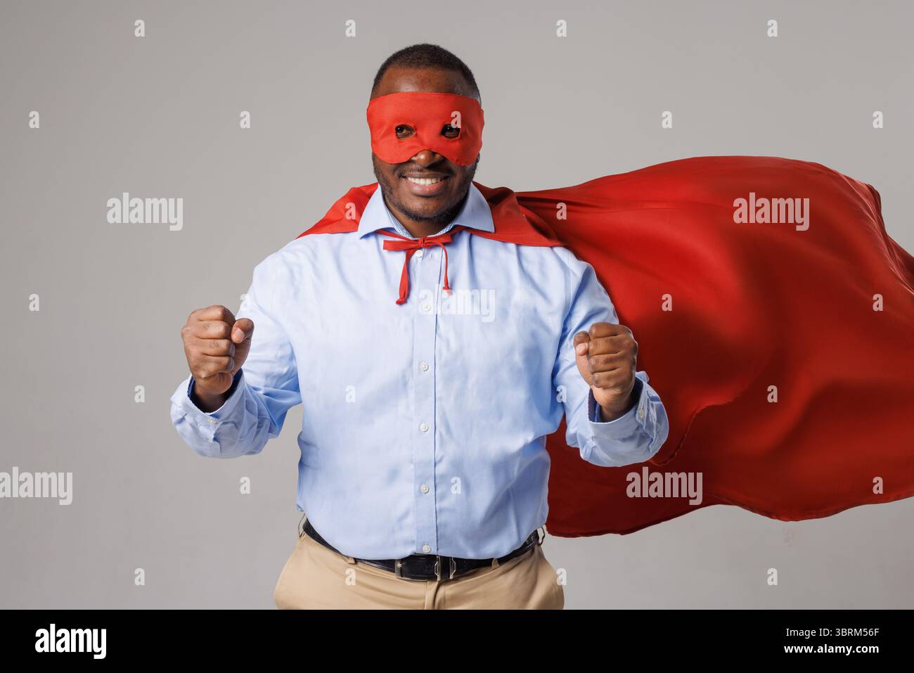 Uomo sorridente in un mantello rosso e maschera che mostra forza e fiducia, simboleggia motivazione e leadership Foto Stock