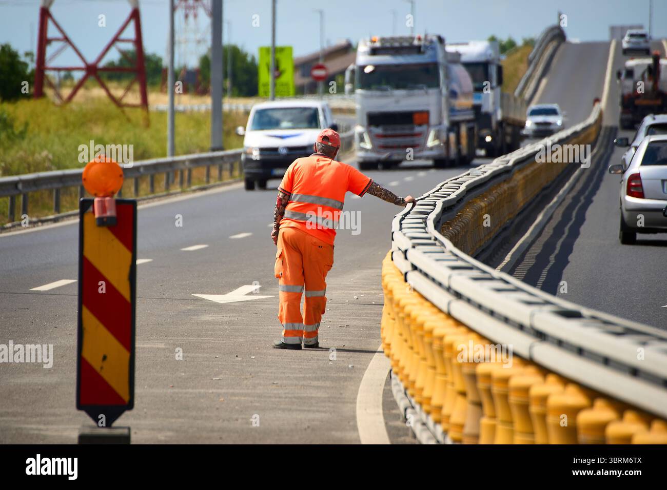 Bragadiru, Romania. 30 giugno 2025: L'operaio devia il traffico per bloccare una rampa dell'incrocio che collega la strada Bucarest-Alessandria con il segmento di Bu Foto Stock