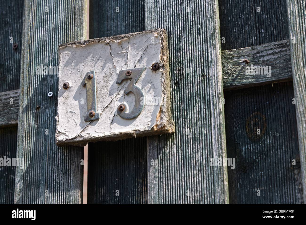 Una casa rustica e intemprata numero '13' su una recinzione di legno angosciata, piena di carattere. Foto Stock