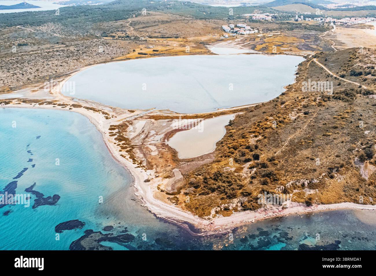 Vista aerea di un lago di acqua salata che si fonde con le acque turchesi del Mar Egeo, mostrando il variegato paesaggio costiero Foto Stock