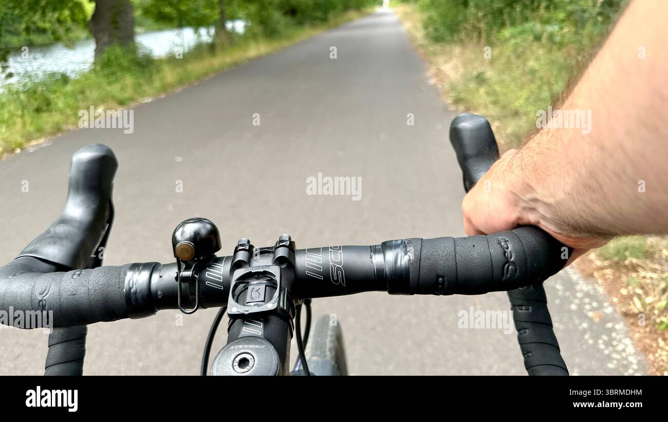 Una strada vista dalla prospettiva di un ciclista su una bicicletta con una mano sul bar Foto Stock
