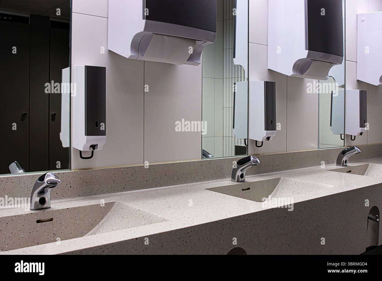 Interno di un moderno bagno pubblico con lavandini multipli con rubinetti automatici cromati, specchi, dispenser di sapone e asciugamani. Foto Stock