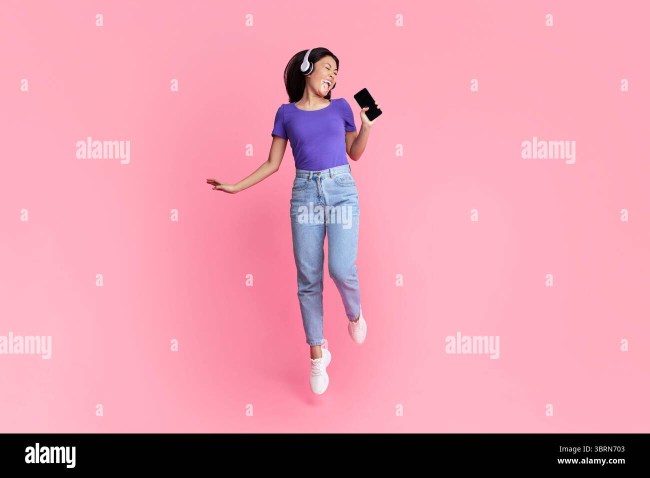 Felice donna asiatica che canta usando lo smartphone come microfono Foto Stock