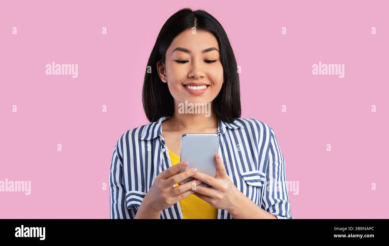 Felice giovane donna asiatica che usa il telefono cellulare in studio Foto Stock