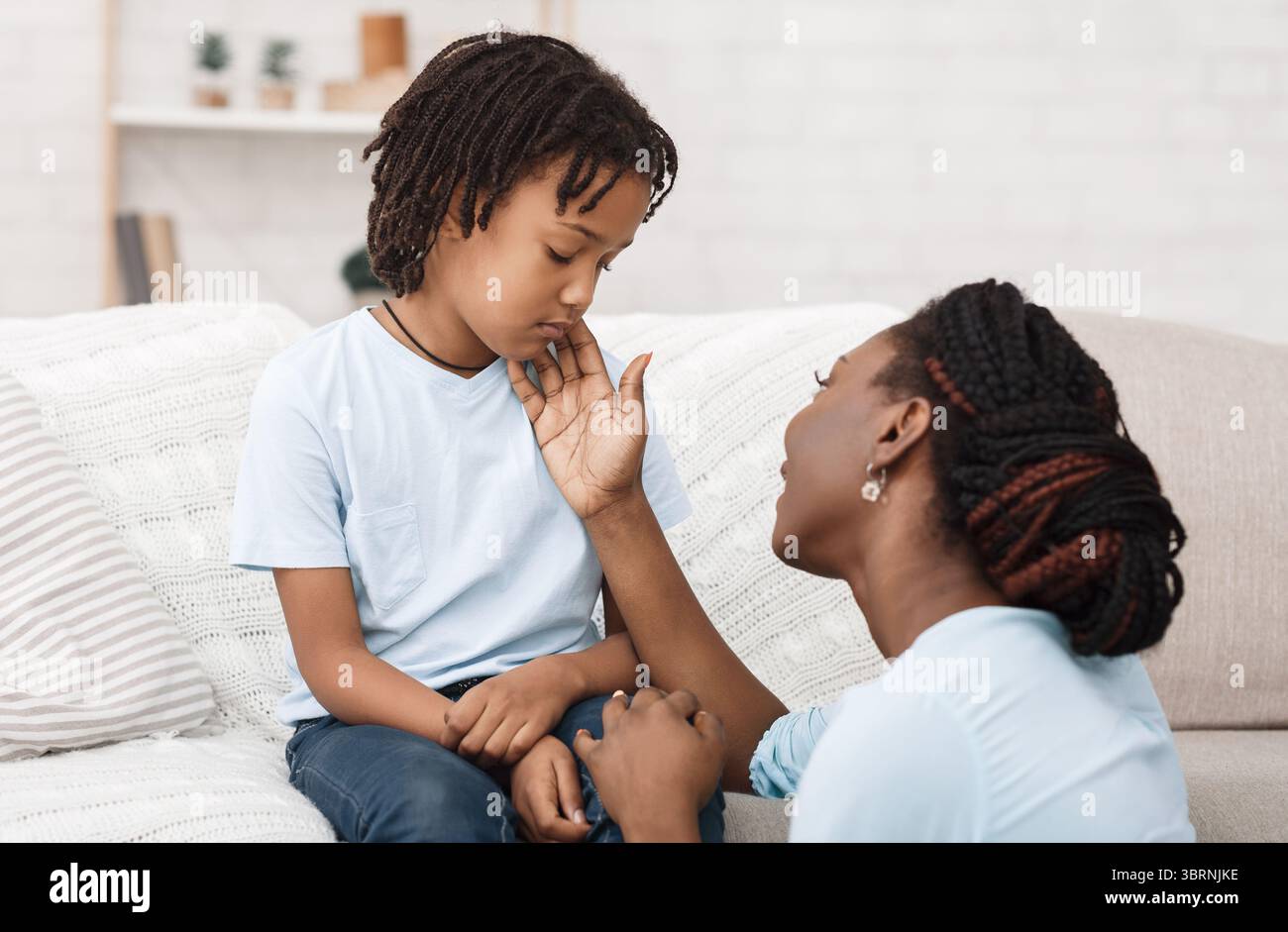 Mamma nera che accarezza il suo bambino depresso sul divano Foto Stock