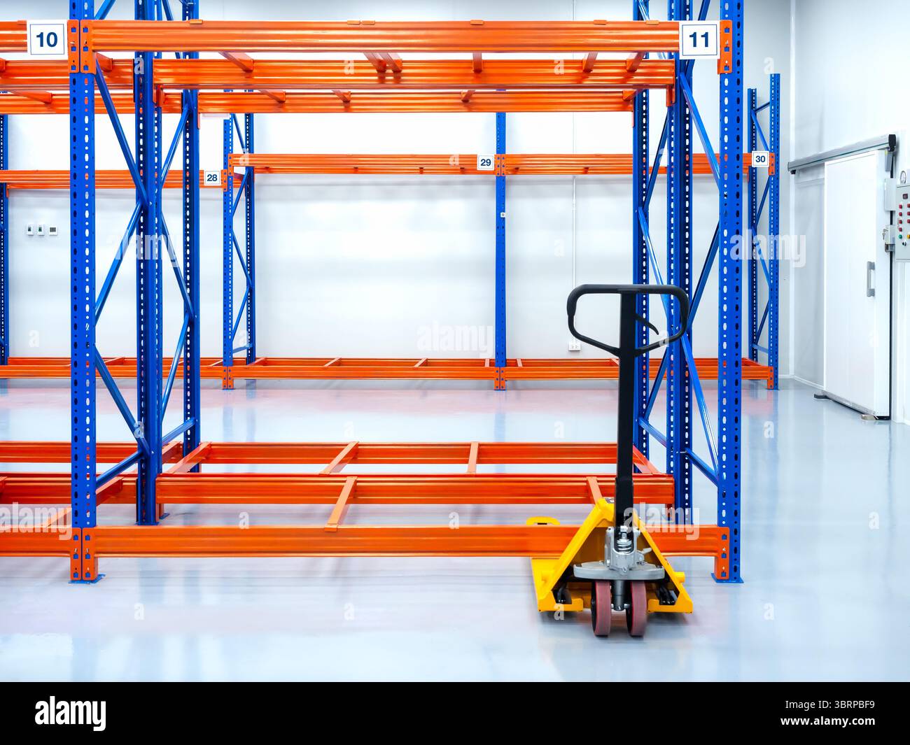 Transpallet manuale giallo o transpallet idraulico, parcheggiato vicino a scaffali, ripiani in acciaio, pronti per il carico delle merci, in magazzino. Sollevamento manuale. Jac. Pallet Foto Stock