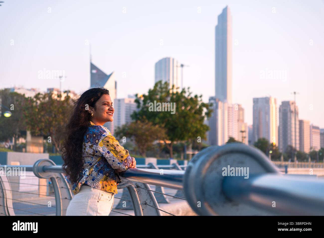 Giovane donna che si gode la vista sulla Corniche di Abu Dhabi con sfondo cittadino Foto Stock