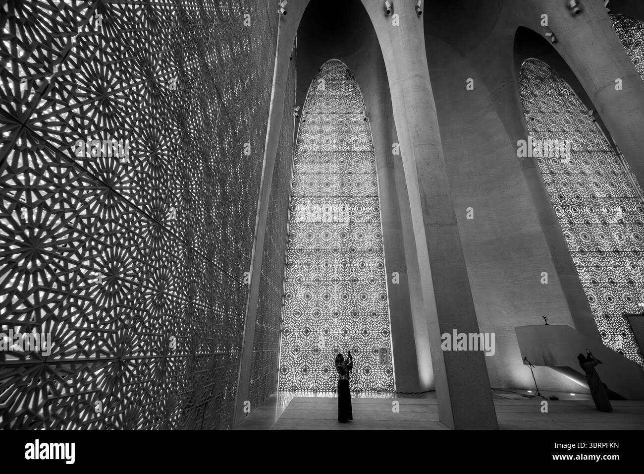 Una donna con un lungo abito si erge in una grande sala con pareti intricate e alti archi, foto interne della grande moschea moderna in bianco e nero Foto Stock