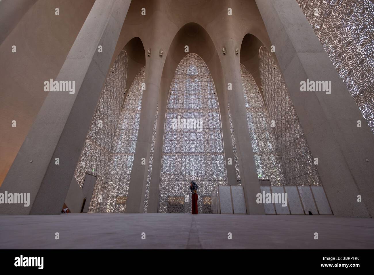 Una persona si trova all'interno di una moschea di casa della famiglia abramitica con alti archi e disegni intricati, con indosso un lungo e modesto vestito Foto Stock