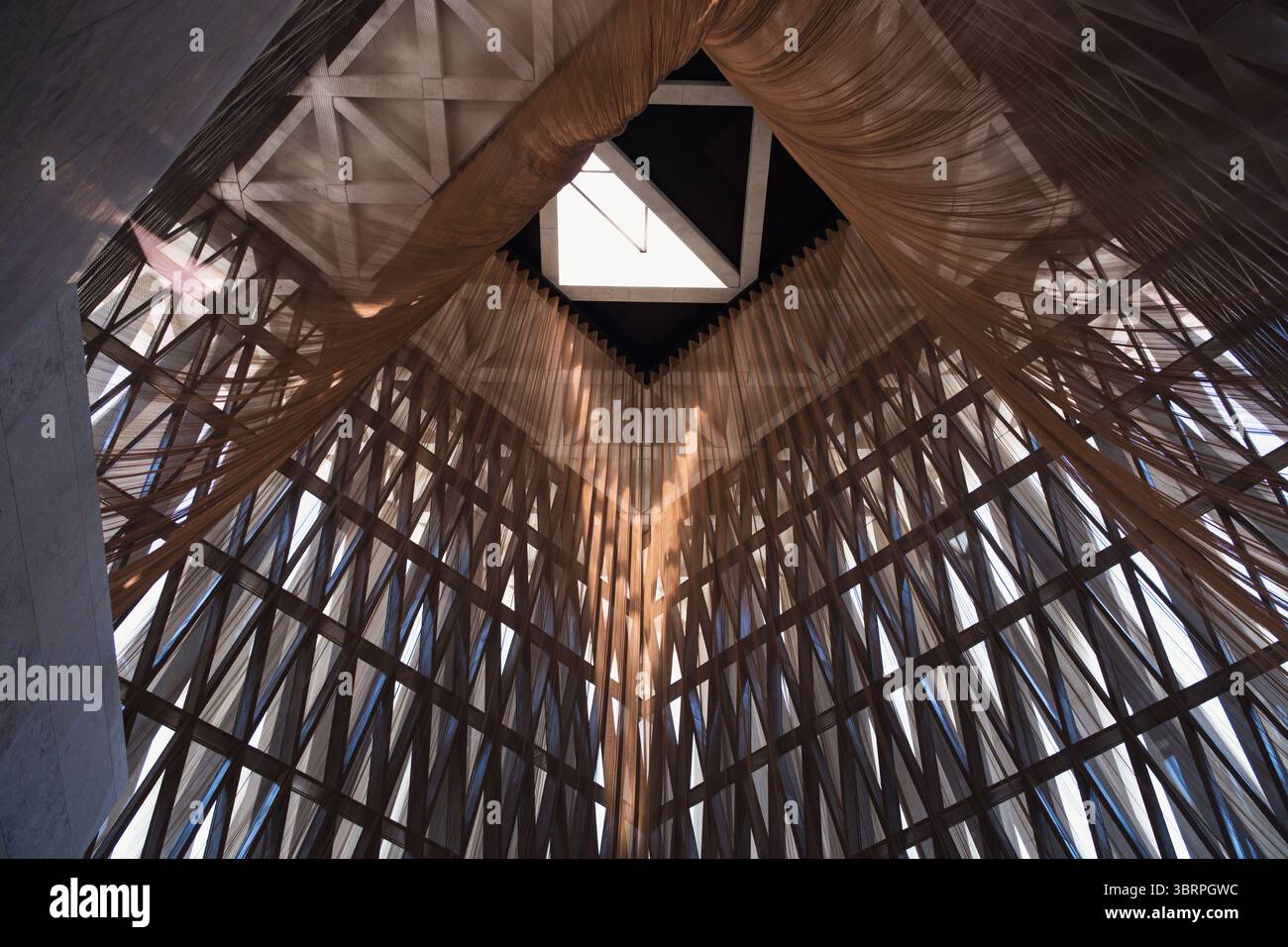 Un vasto e artistico interno architettonico con intricati motivi a griglia in legno e lucernario, che creano spettacolari effetti di luce ed ombra. Foto Stock