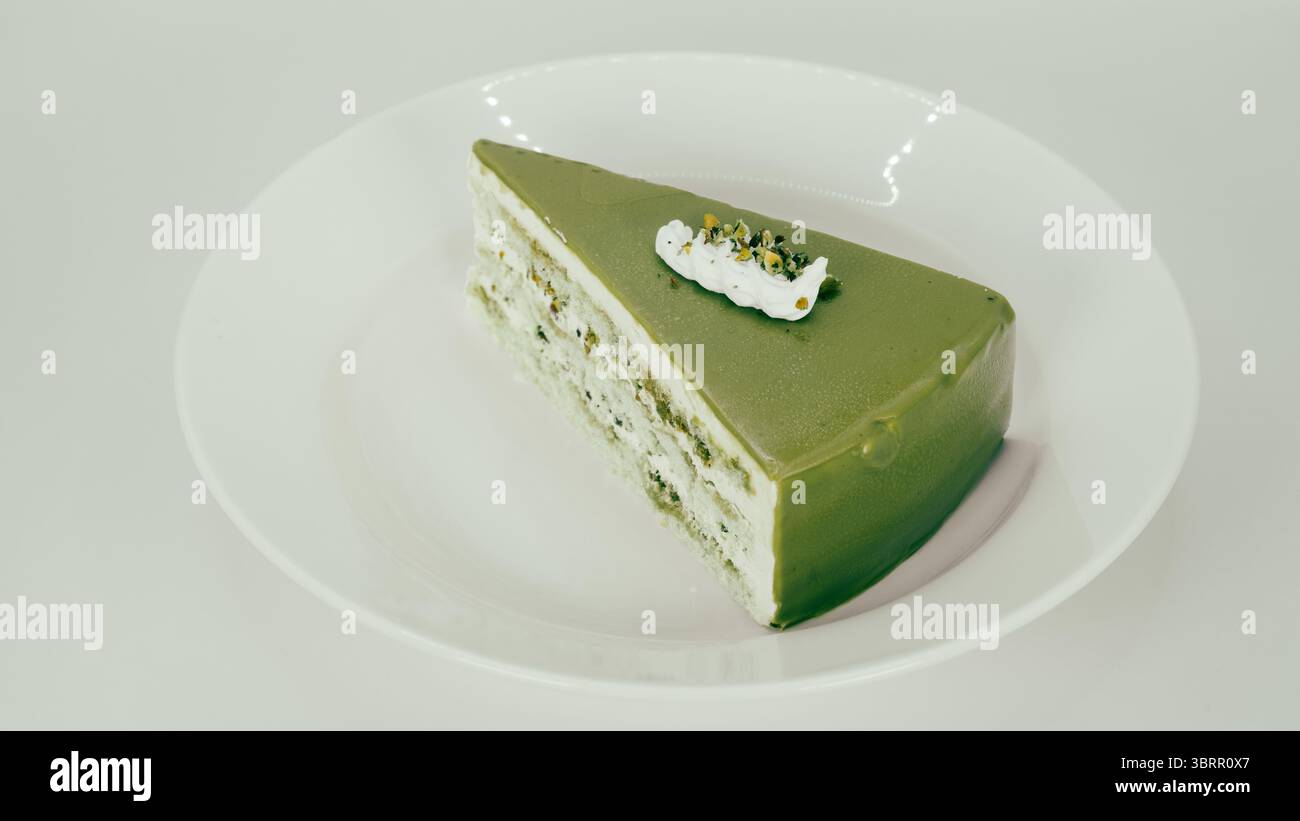 Una fetta di torta verde matcha condita con una piccola dose di panna e guarnita con pistacchi schiacciati, una fetta di torta al cioccolato virale di Dubai su un whi Foto Stock