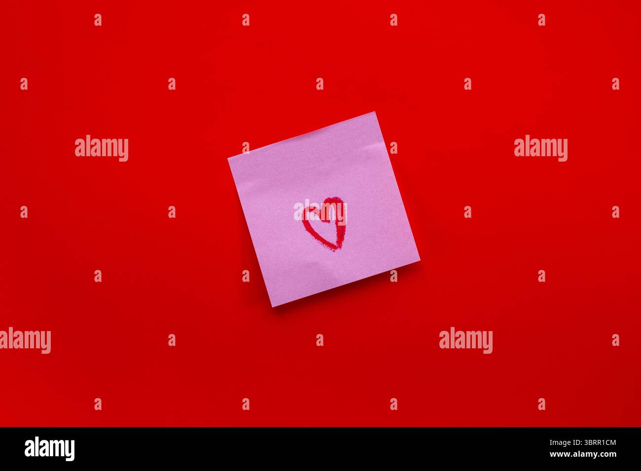 Cuore rosso disegnato a mano su una nota adesiva su uno sfondo rosso intenso Foto Stock