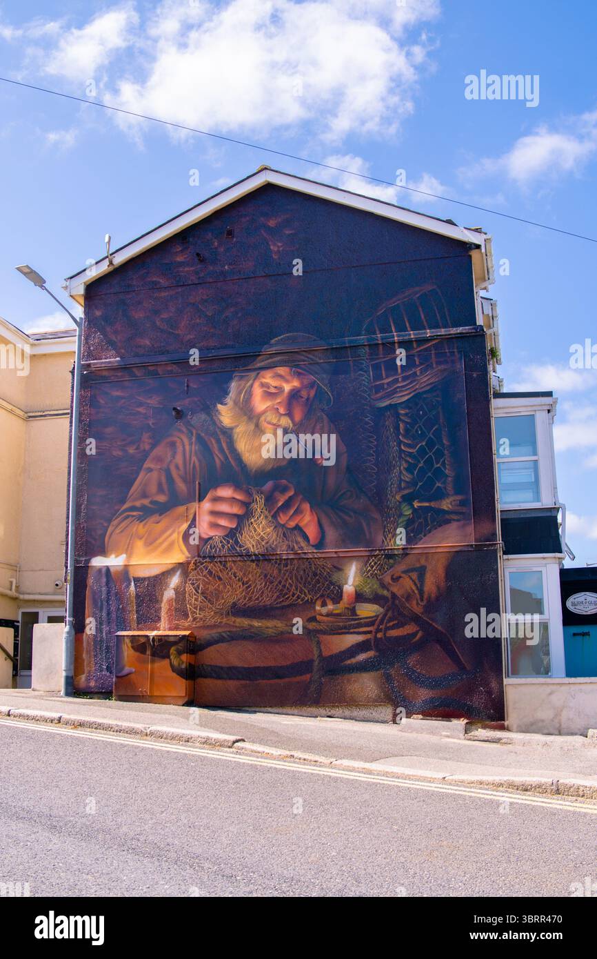 Vivace murale di un tradizionale pescatore della Cornovaglia che muta le reti a lume di candela, dipinto sul lato di un edificio a Newquay, Cornovaglia, Regno Unito. Foto Stock