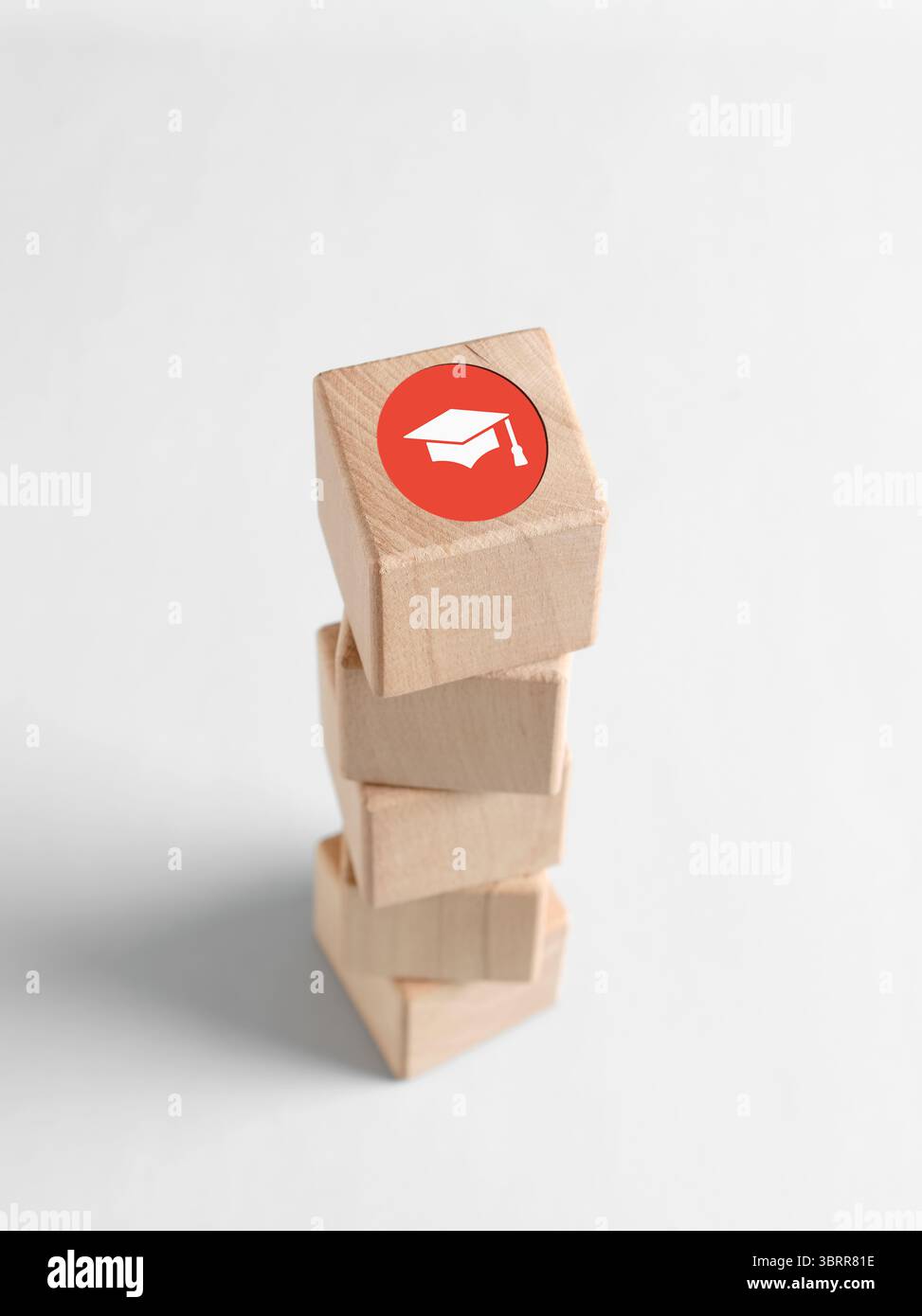 Cubi di legno impilati con un'icona con un cappello graduato sulla parte superiore, che simboleggia il successo accademico e la ricerca dell'istruzione superiore Foto Stock