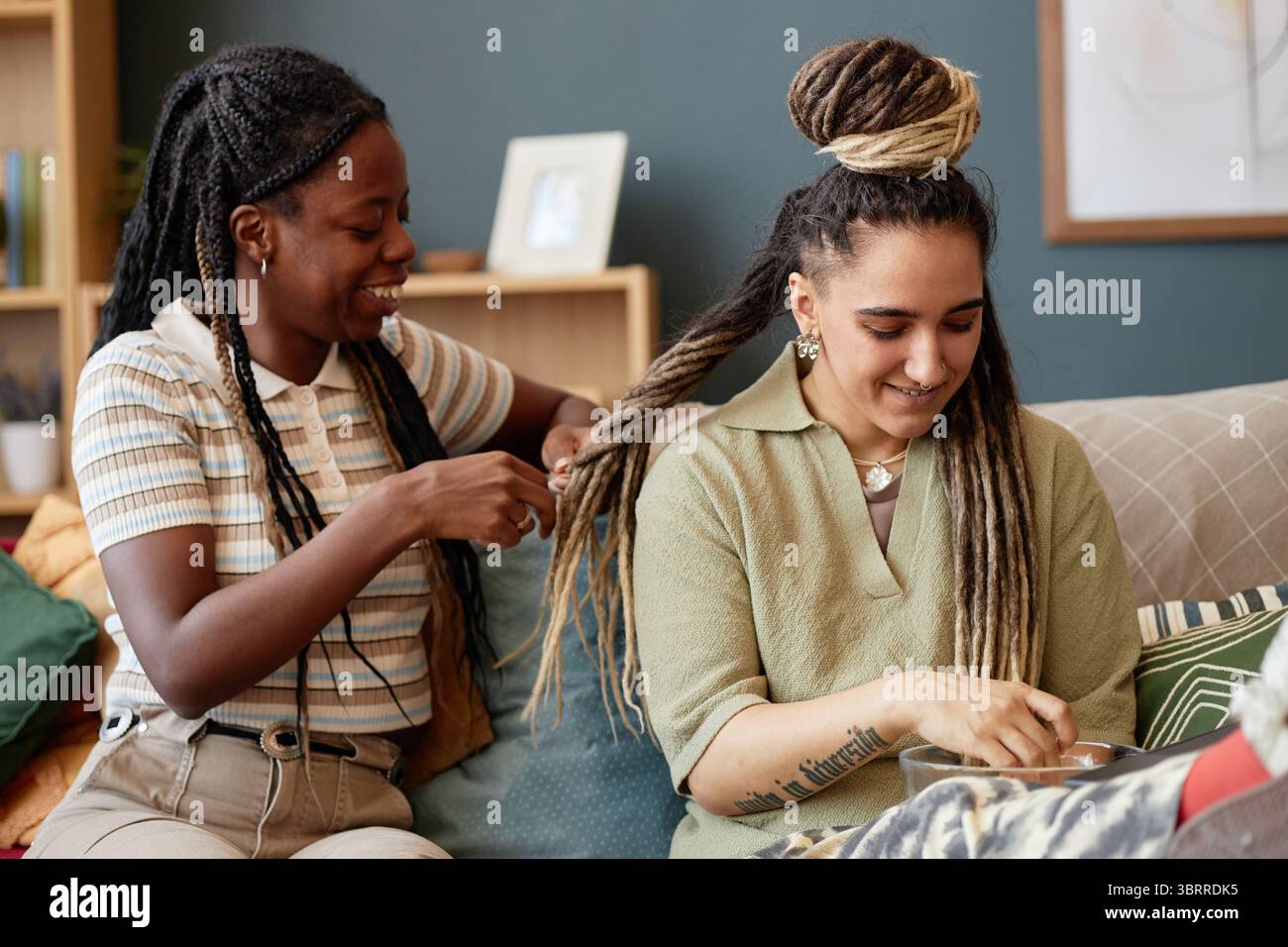 Giovane donna nera capelli intrecciati di giovane donna caucasica seduta al chiuso Foto Stock