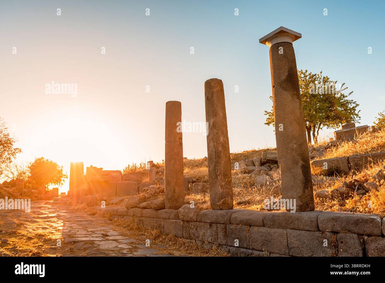 Resti dell'antica civiltà ad Assos, Behramkale, Turchia, con una strada in pietra e colonne al tramonto Foto Stock